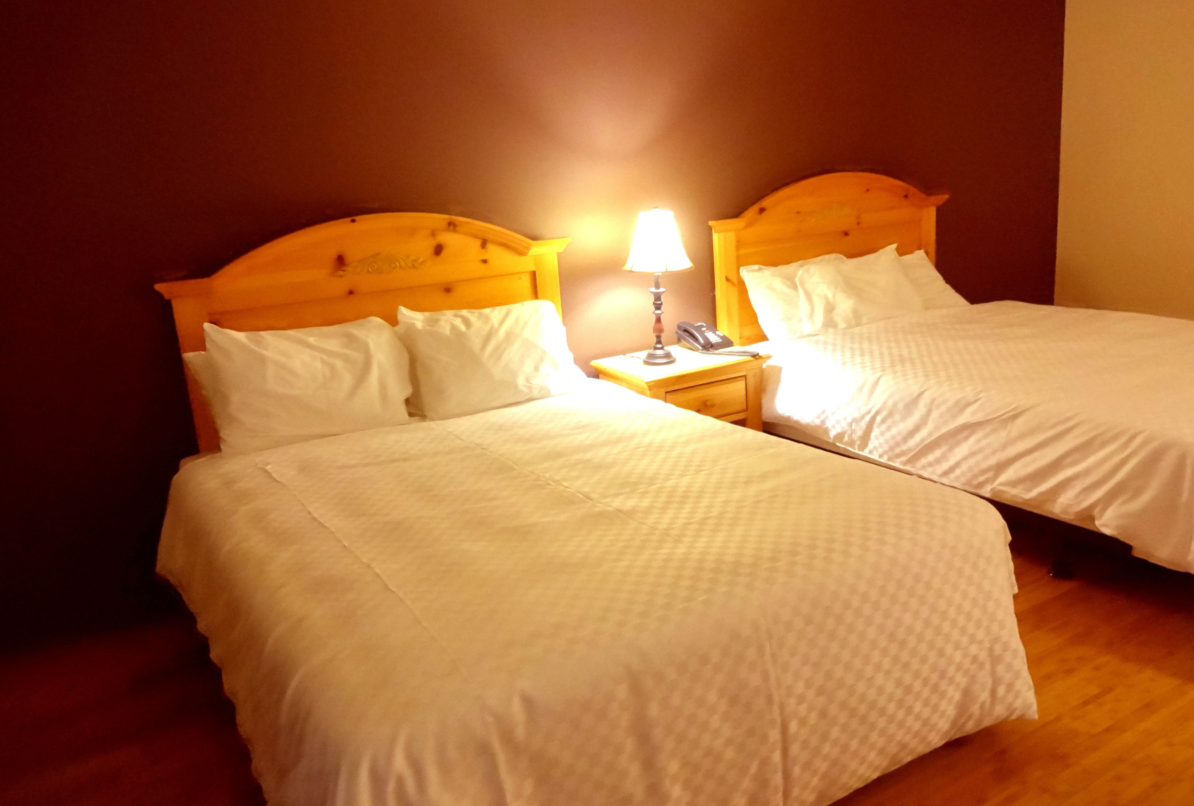 Two single beds with wooden headboards, white bedding, and a bedside table with a lamp and phone.