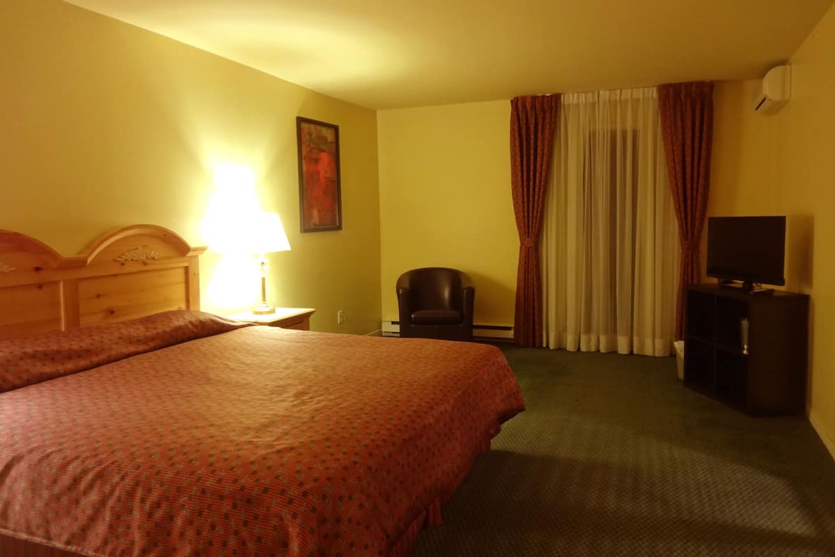 A hotel room with a large bed, a chair, a television, and a window with curtains.