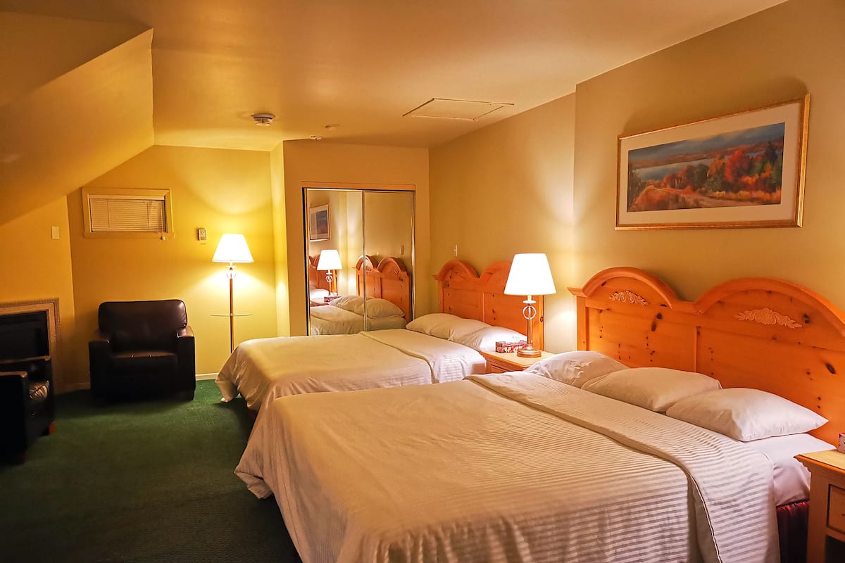 A hotel room with two beds, a chair, a desk, and a painting on the wall.