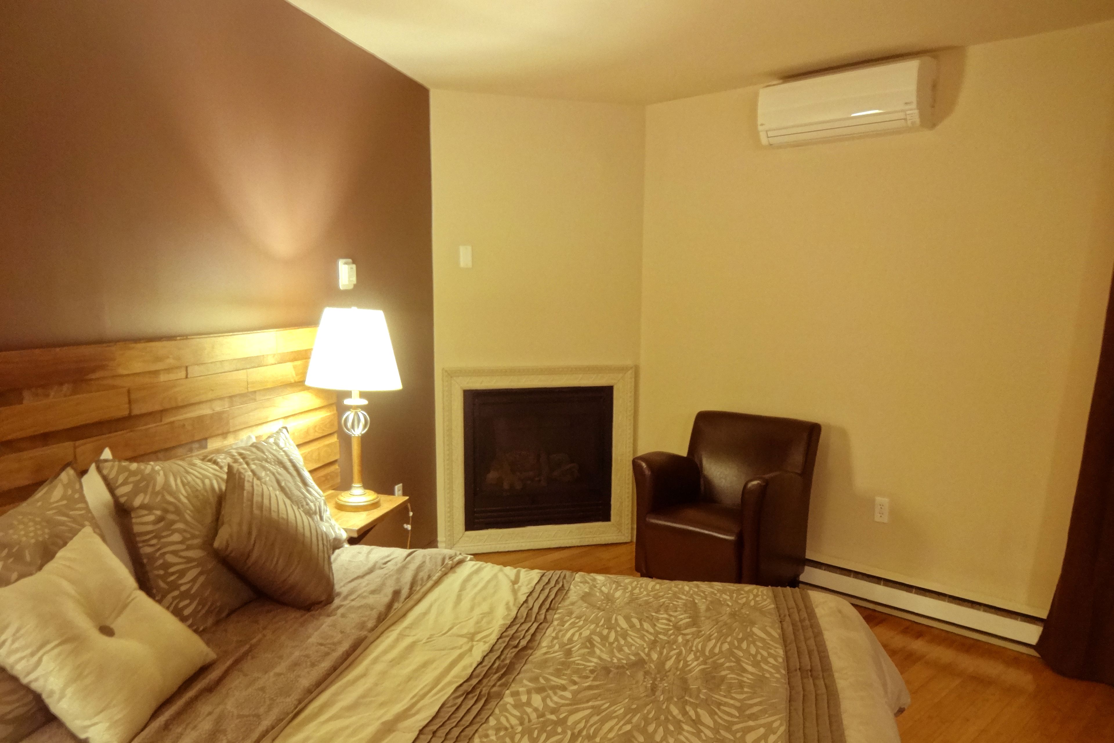 A hotel room with a bed, a nightstand with a lamp, a fireplace, and a leather chair.