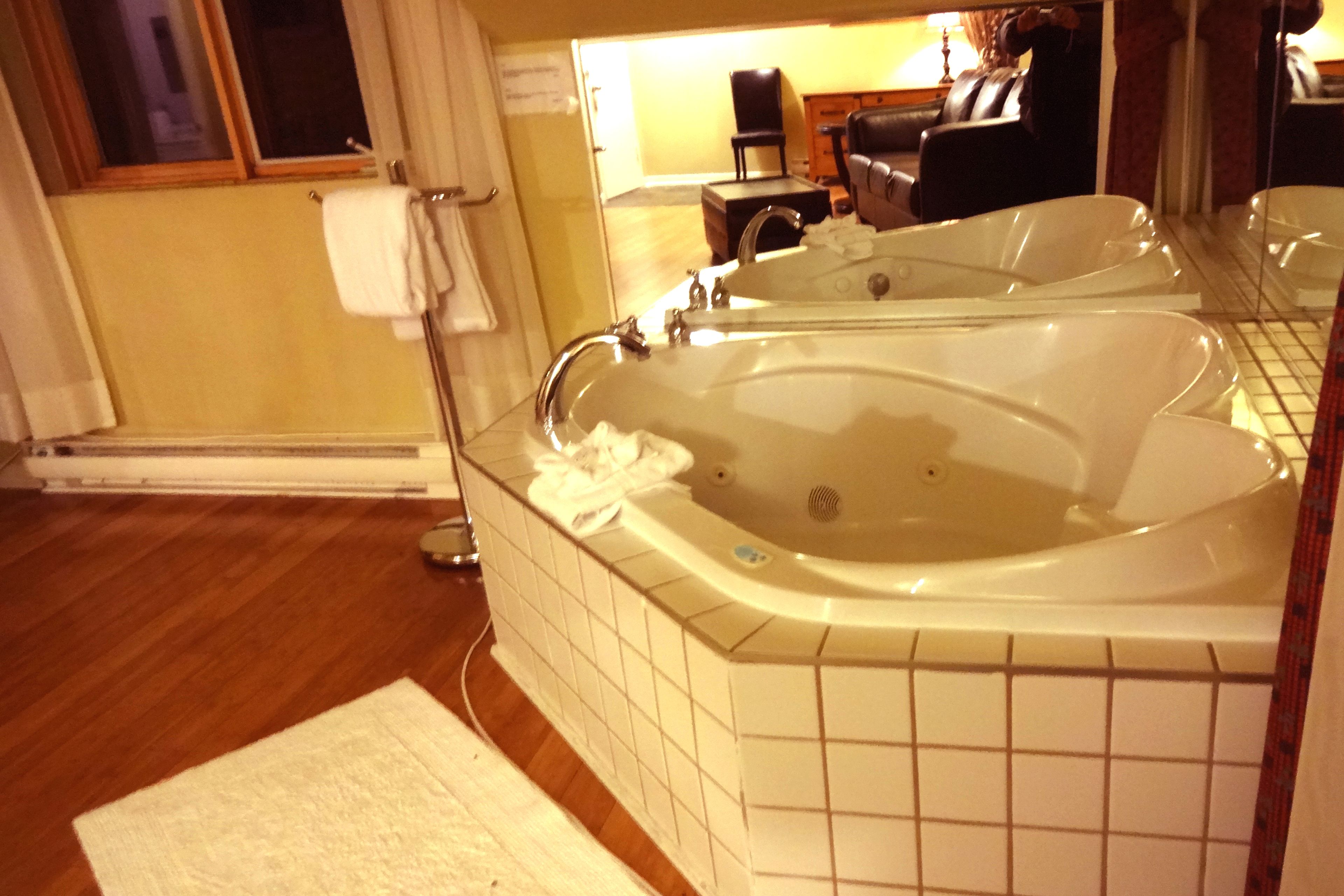 Un bagno con due vasche da bagno ampie, un pavimento in legno e una parete rivestita in piastrelle.