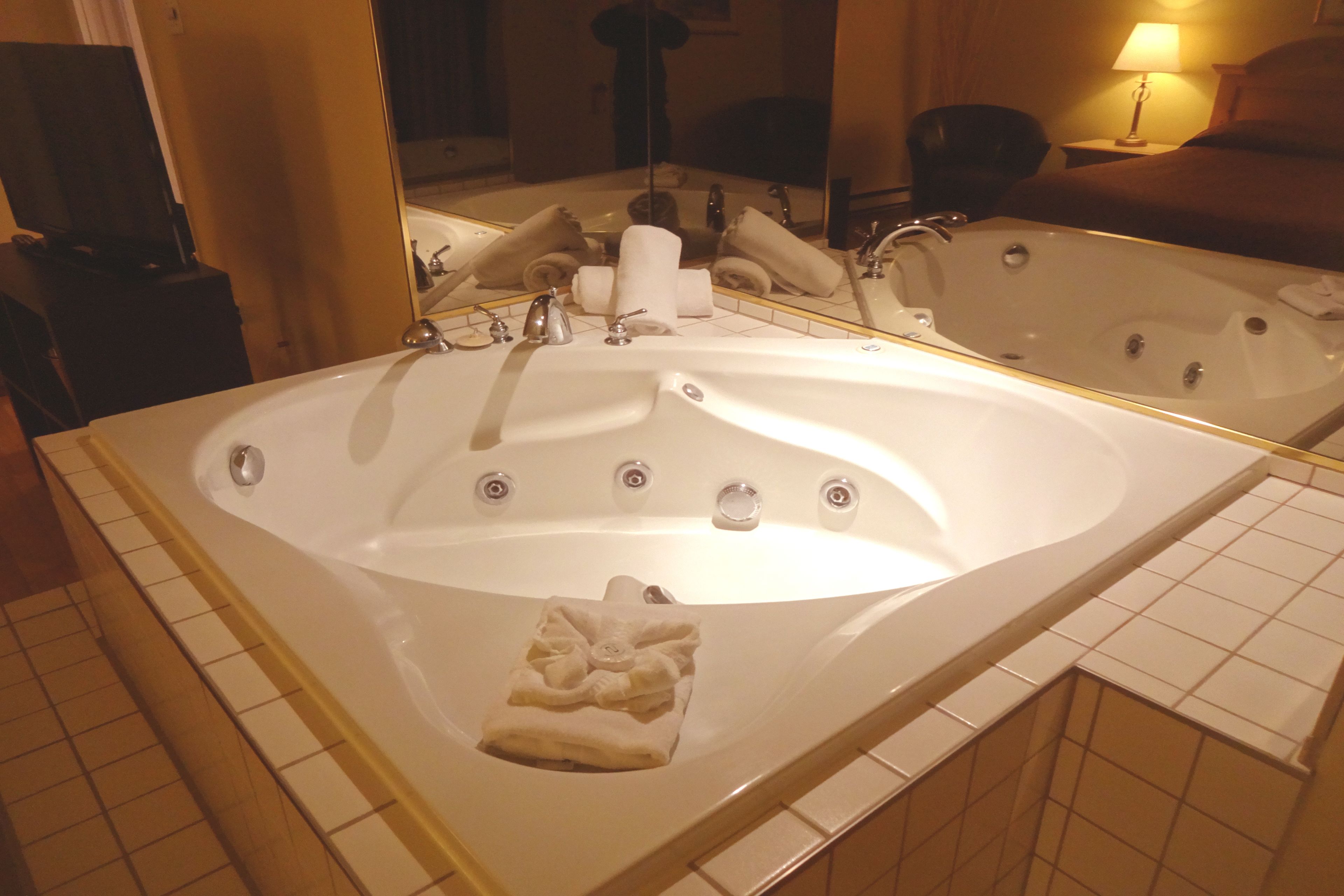 Una bañera grande y rectangular con múltiples grifos y un espejo encima.