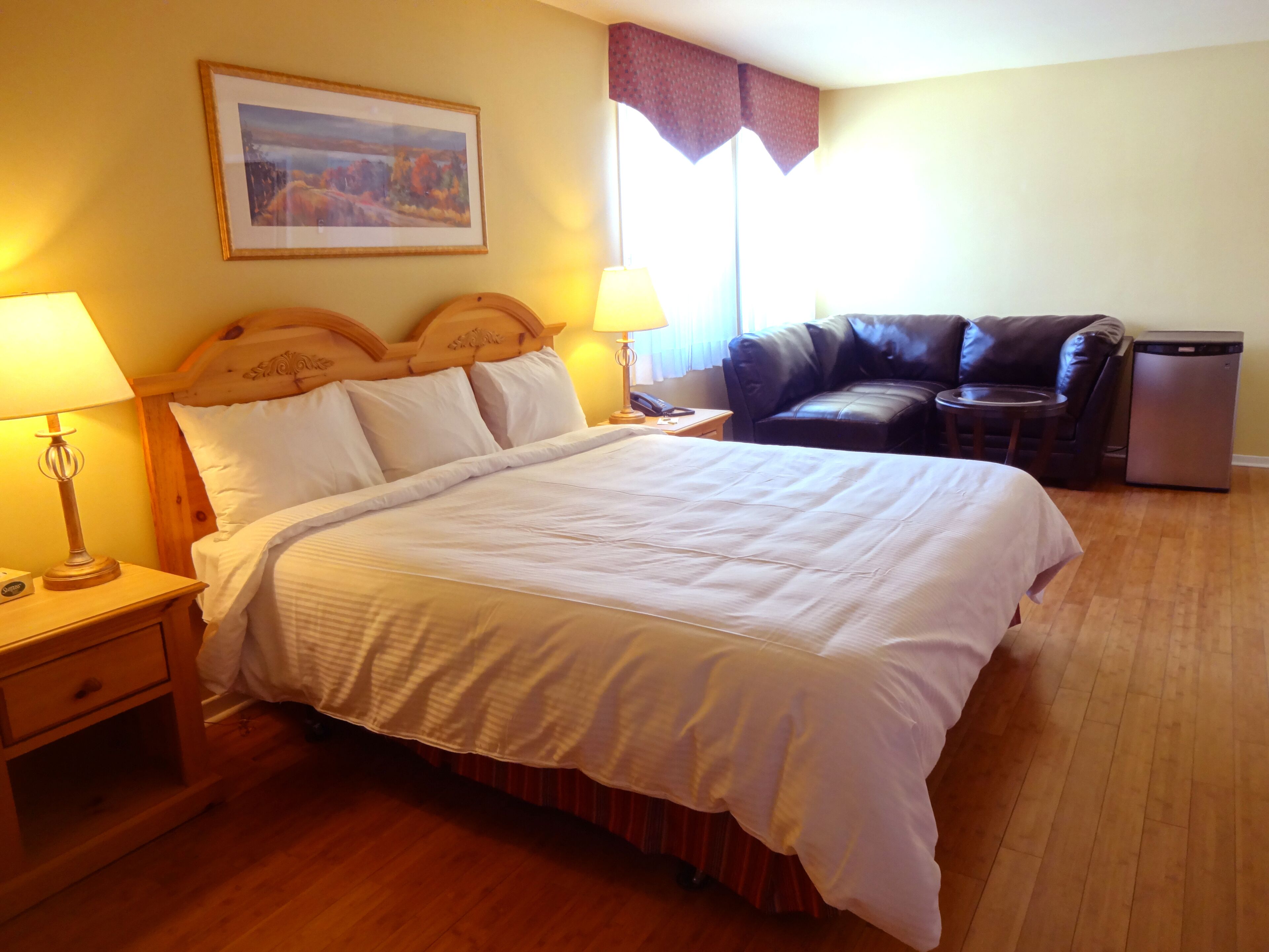A neatly made bed with a wooden headboard, a bedside table with a lamp, a leather armchair, and a small table with a phone.