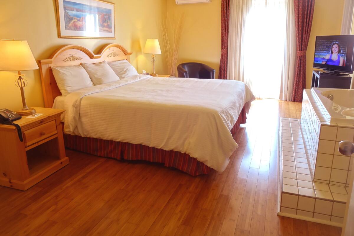 A hotel room with a large bed, bedside lamps, a desk with a telephone, a TV, and a bathtub.