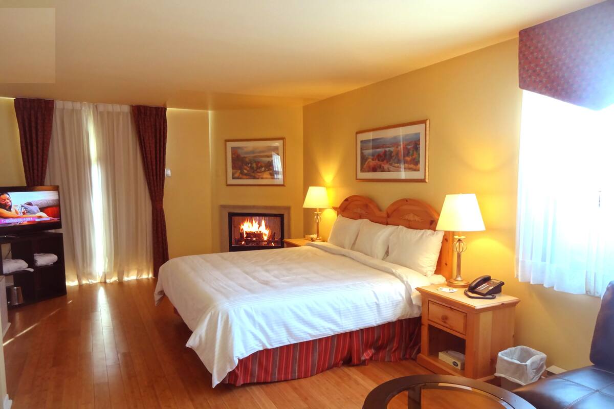 A hotel room with a bed, a fireplace, a television, a desk, a chair, and a round table.