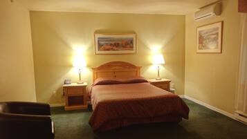 A hotel room with a bed, two bedside lamps, a wooden headboard, a nightstand, a chair, and a painting on the wall.