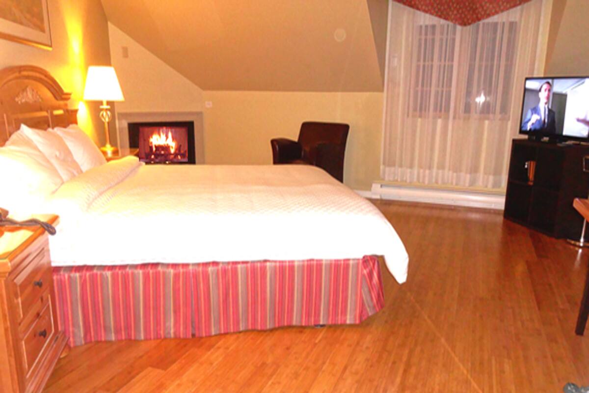 A hotel room with a large bed, a fireplace, a television, and a wooden floor.