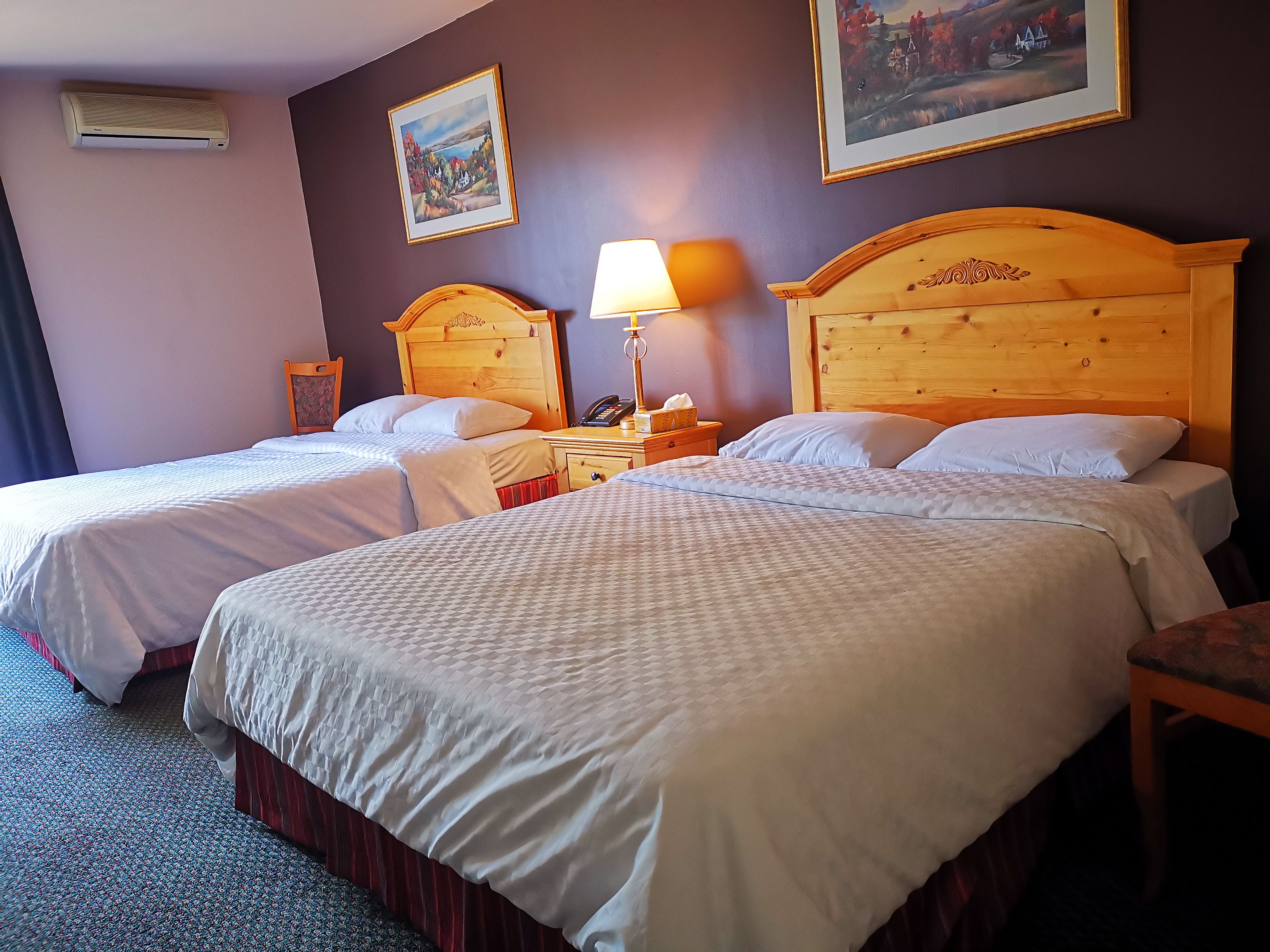 A hotel room with two beds, a nightstand with a lamp, a telephone, and a painting on the wall.