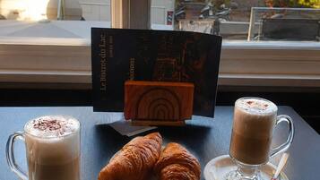 A table with two cups of coffee, two croissants, and a menu card.
