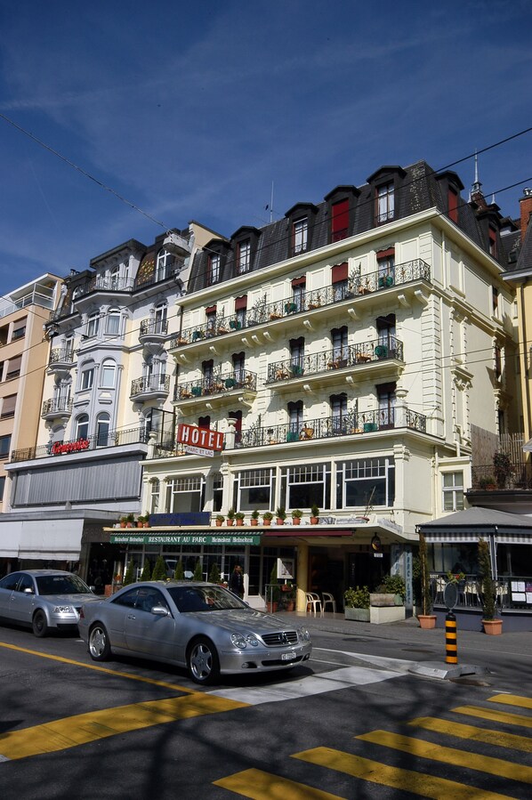 A multi-story hotel with balconies, a restaurant at the ground level, and a car in the foreground. - Hotel Parc & Lac (Montreux)