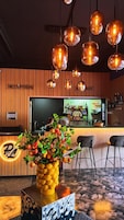 Zona de recepción con pared de madera, mostrador de recepción, área de bar y un centro de mesa con plantas.