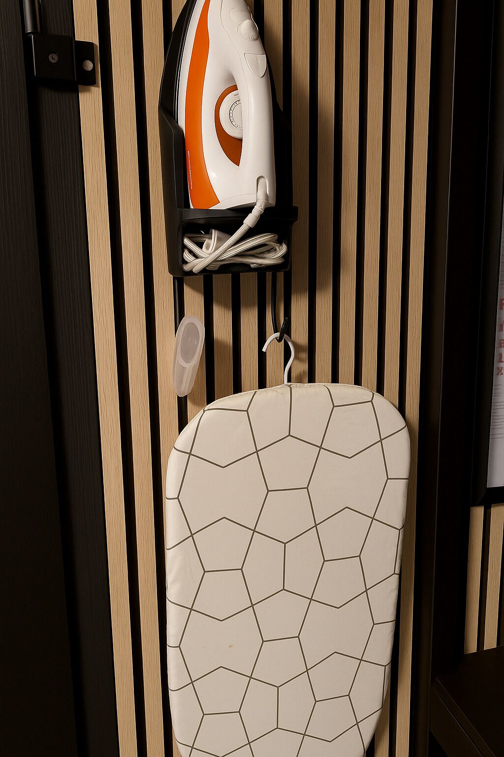 Un baño con pared de listones de madera, un inodoro blanco con diseño de azulejos geométricos y un radiador naranja y blanco sobre una estantería.