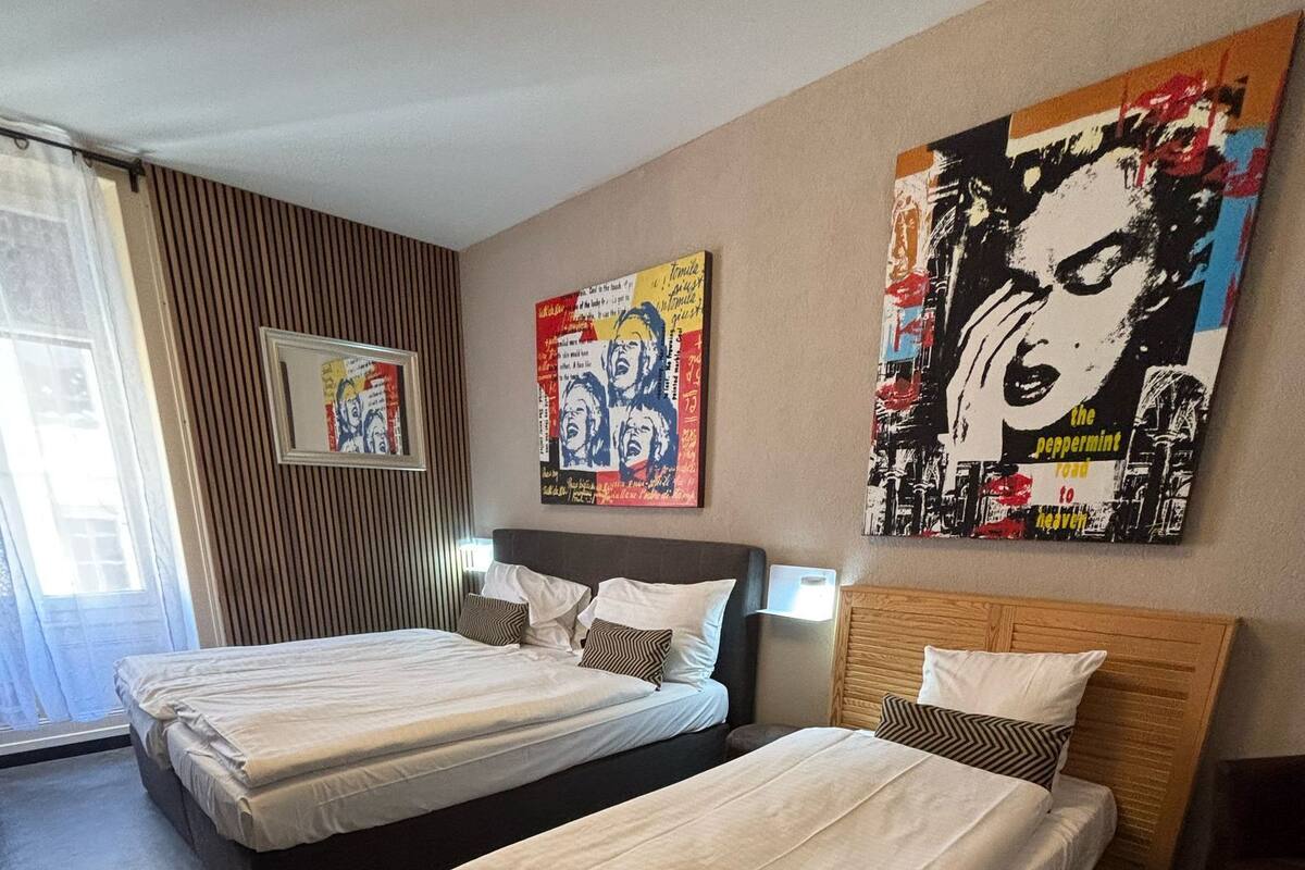 A hotel room with two single beds, a wooden headboard, a large poster on the wall, and a window with curtains.