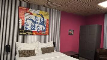 Ein Schlafzimmer mit einem Bett, einem Wandbild, einem Kleiderschrank und einem Sessel.