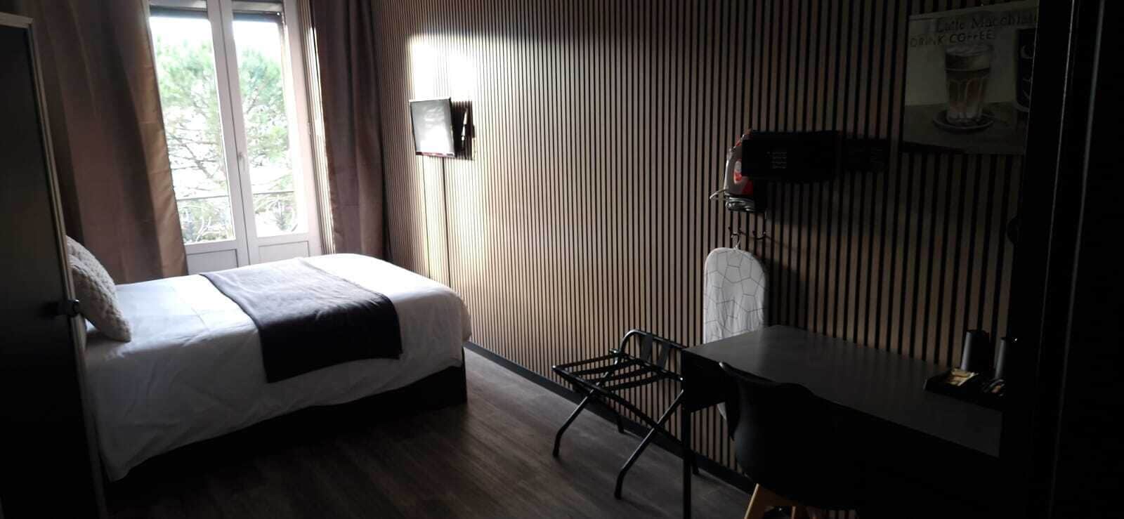 A hotel room with a bed, a desk, a chair, a window with curtains, and a sign offering coffee.