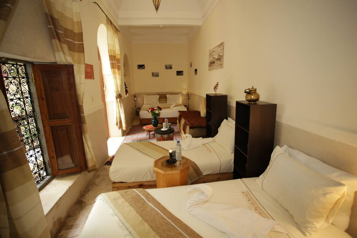 A hotel room with two beds, a wooden nightstand, a small table with a water bottle, and a decorative item on the nightstand.
