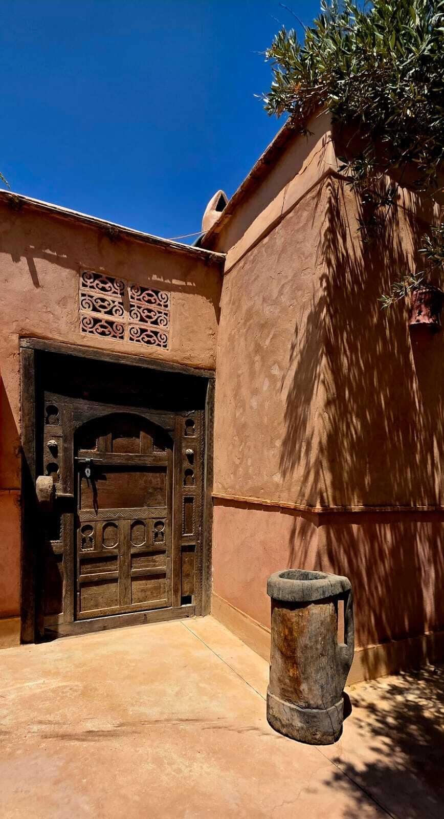 Um edifício tradicional com uma grande porta de madeira, uma pequena janela com padrões decorativos e uma estrutura de concreto à frente.