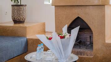 A cozy living room with a fireplace, a potted plant, and a small table with water bottles and a bouquet of flowers.