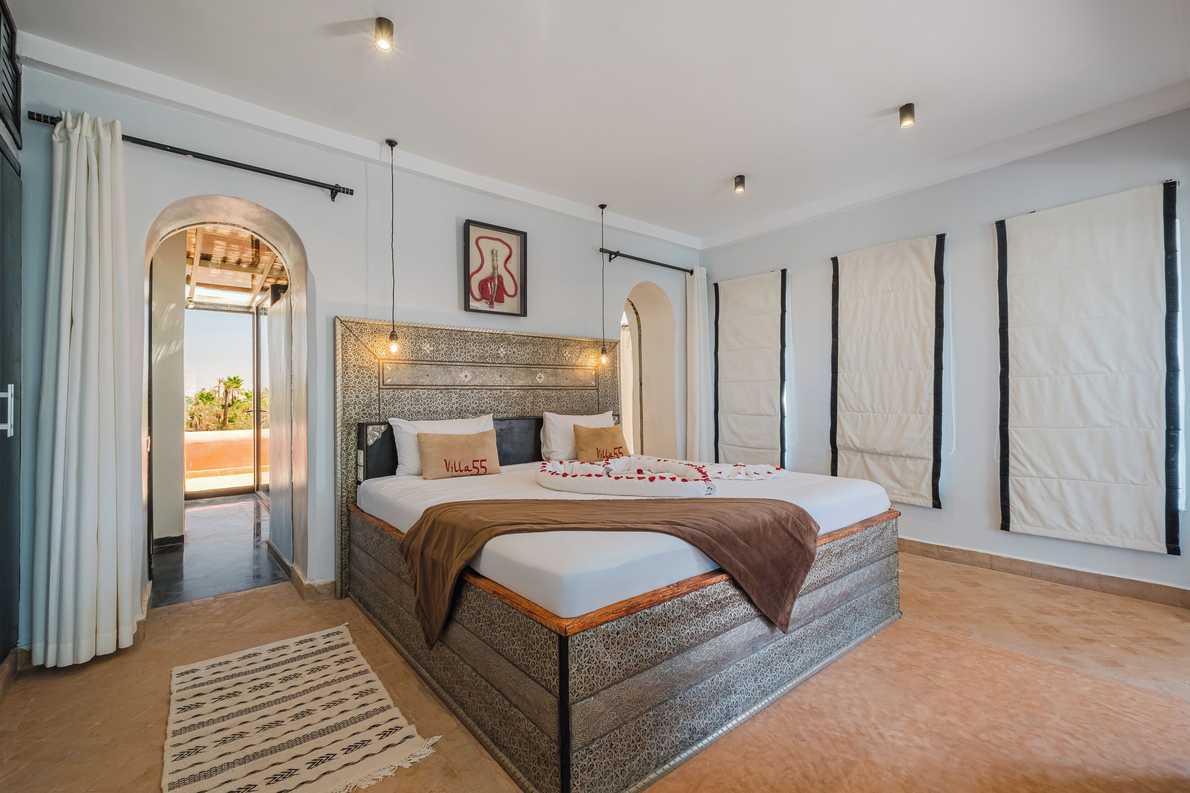 Een ruime slaapkamer met een groot bed, een gestreept hoofdeinde en uitzicht door een boog naar buiten.