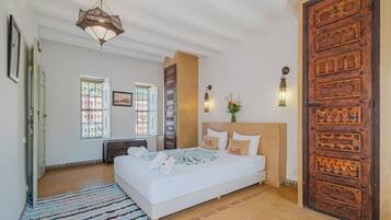 A spacious bedroom with a large bed, a wooden door, and a decorative ceiling light.