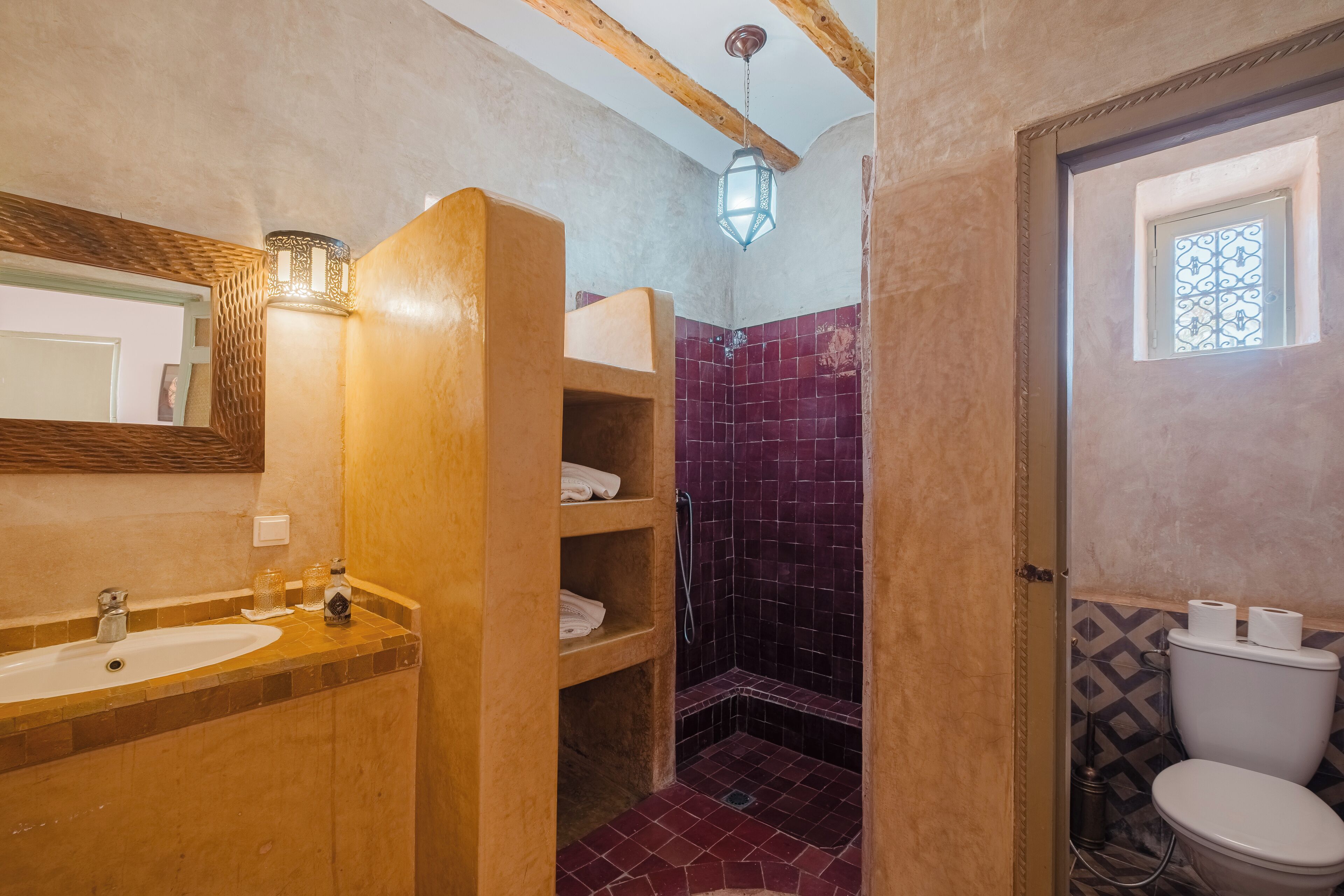 A bathroom with a wooden vanity, a sink, a shower with purple tiles, and a toilet.