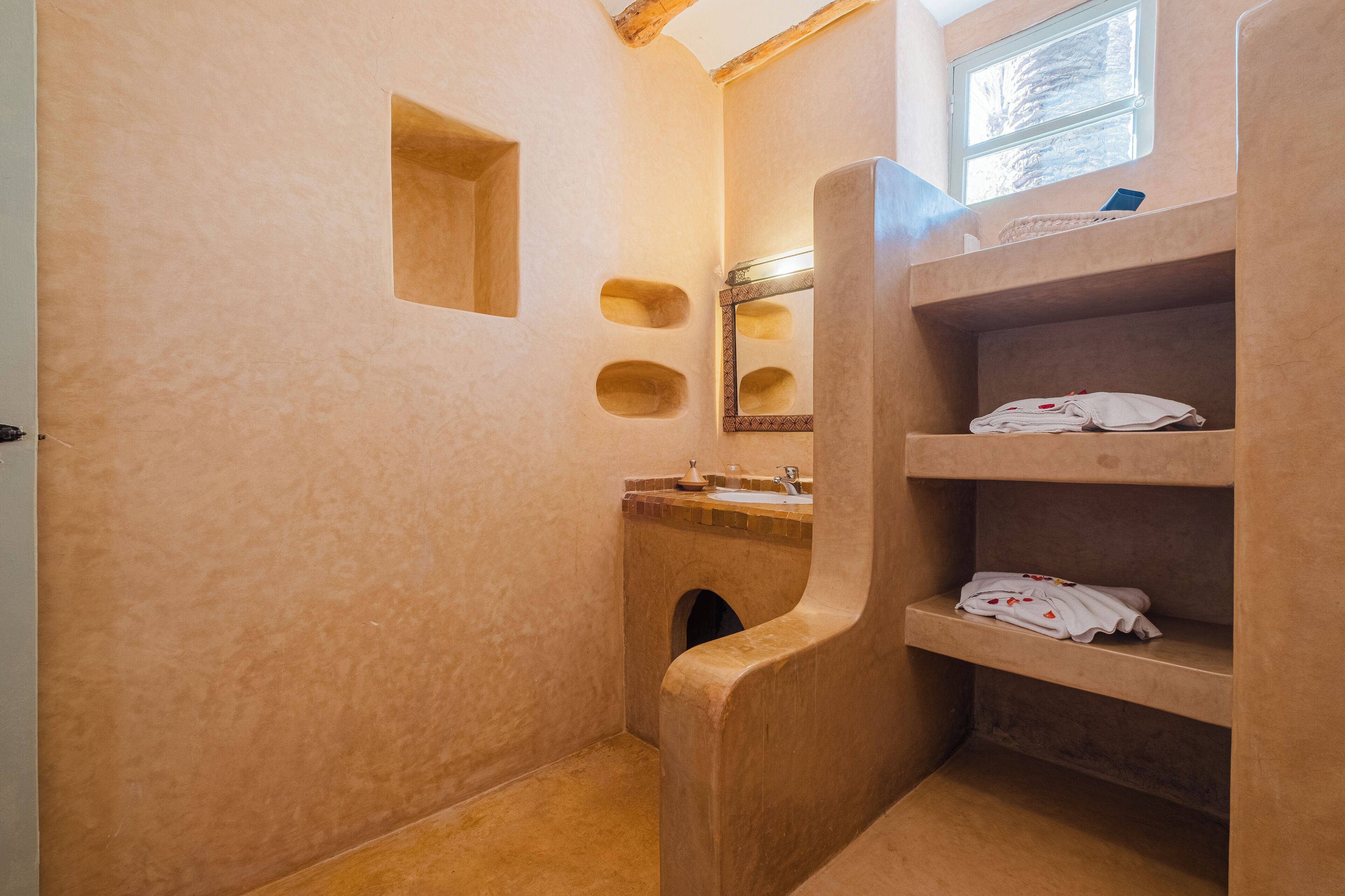A bathroom with a unique architectural design, featuring a wooden vanity with a mirror and shelves for towels.