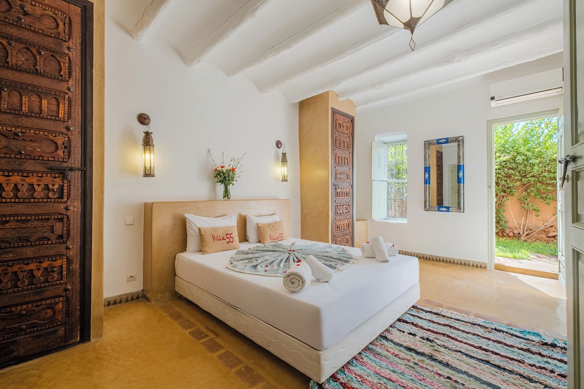 Un dormitorio con una cama grande, una puerta de madera, una lámpara fijada a la pared y una ventana.