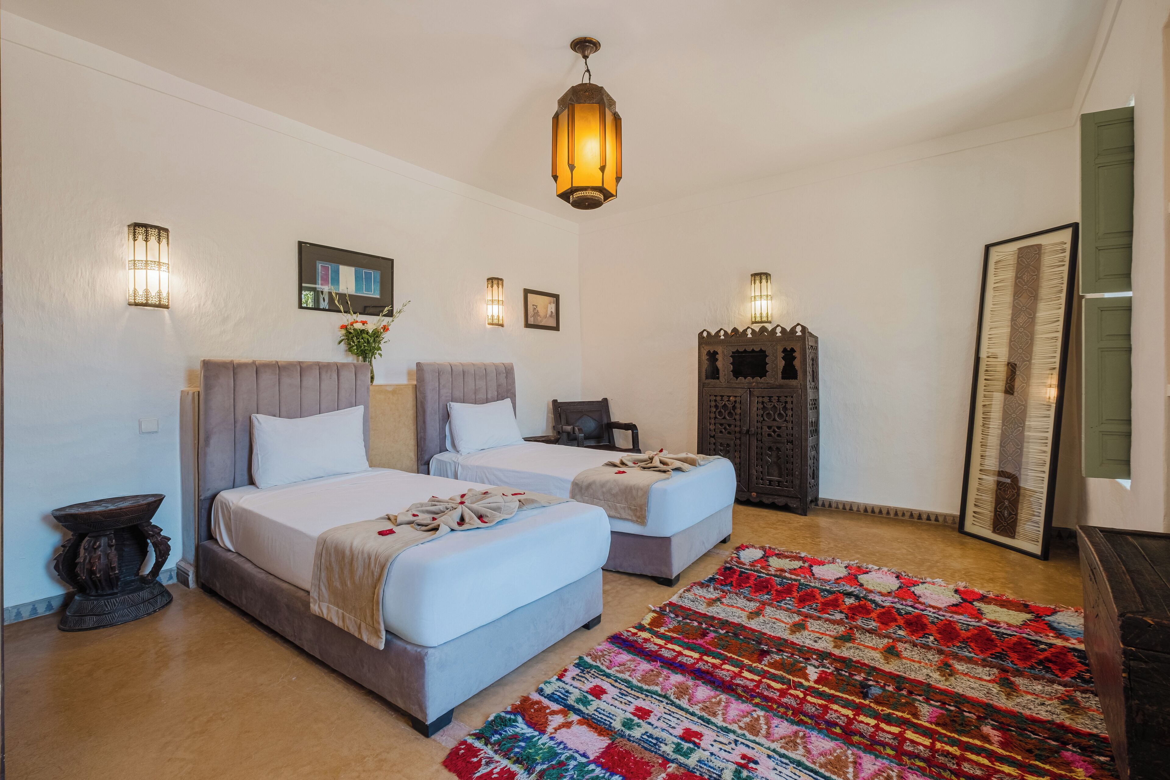 A hotel room with two beds, a large mirror, a decorative rug, and wall-mounted lights.
