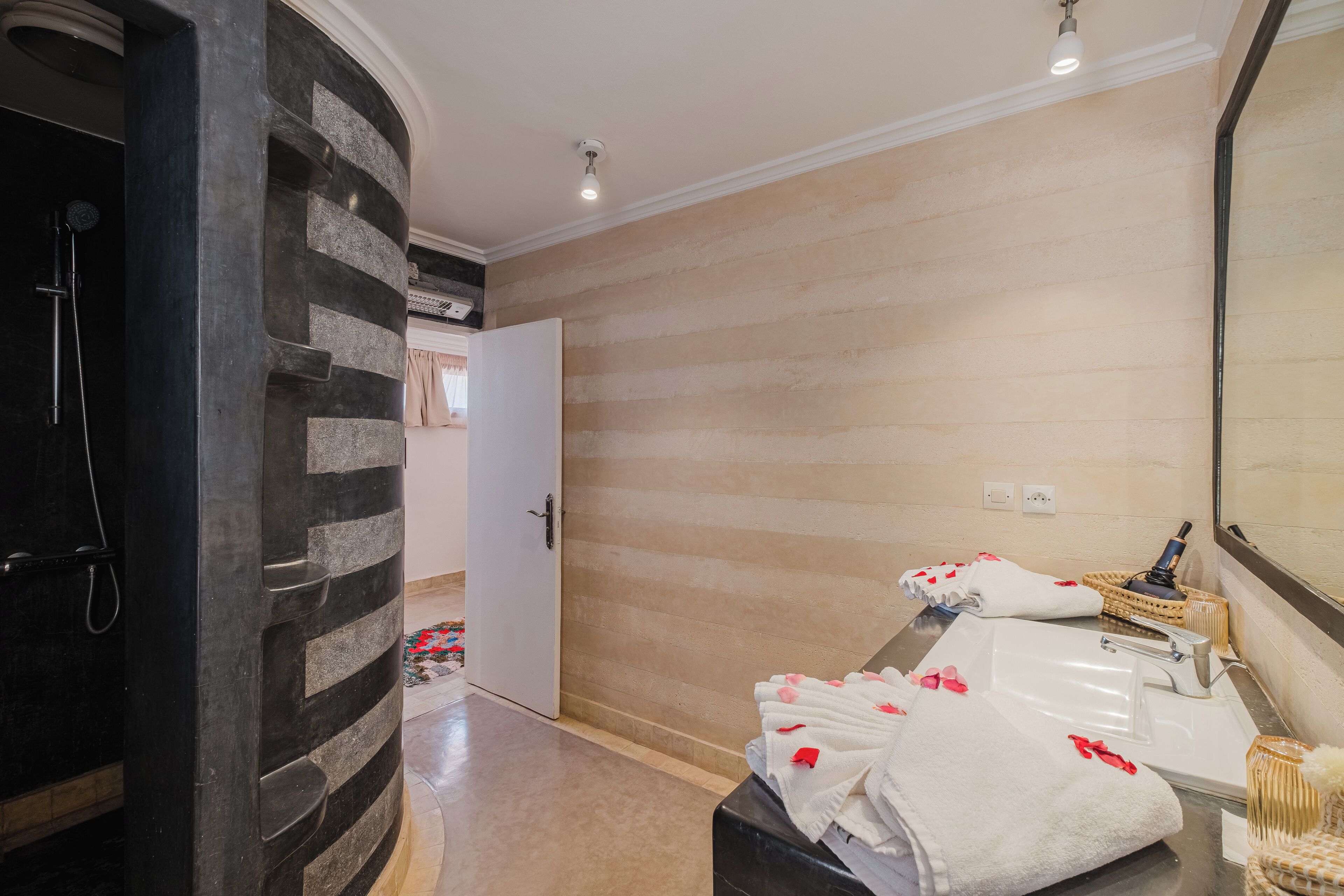 Un baño con pared de piedra, ducha, lavamanos y espejo.