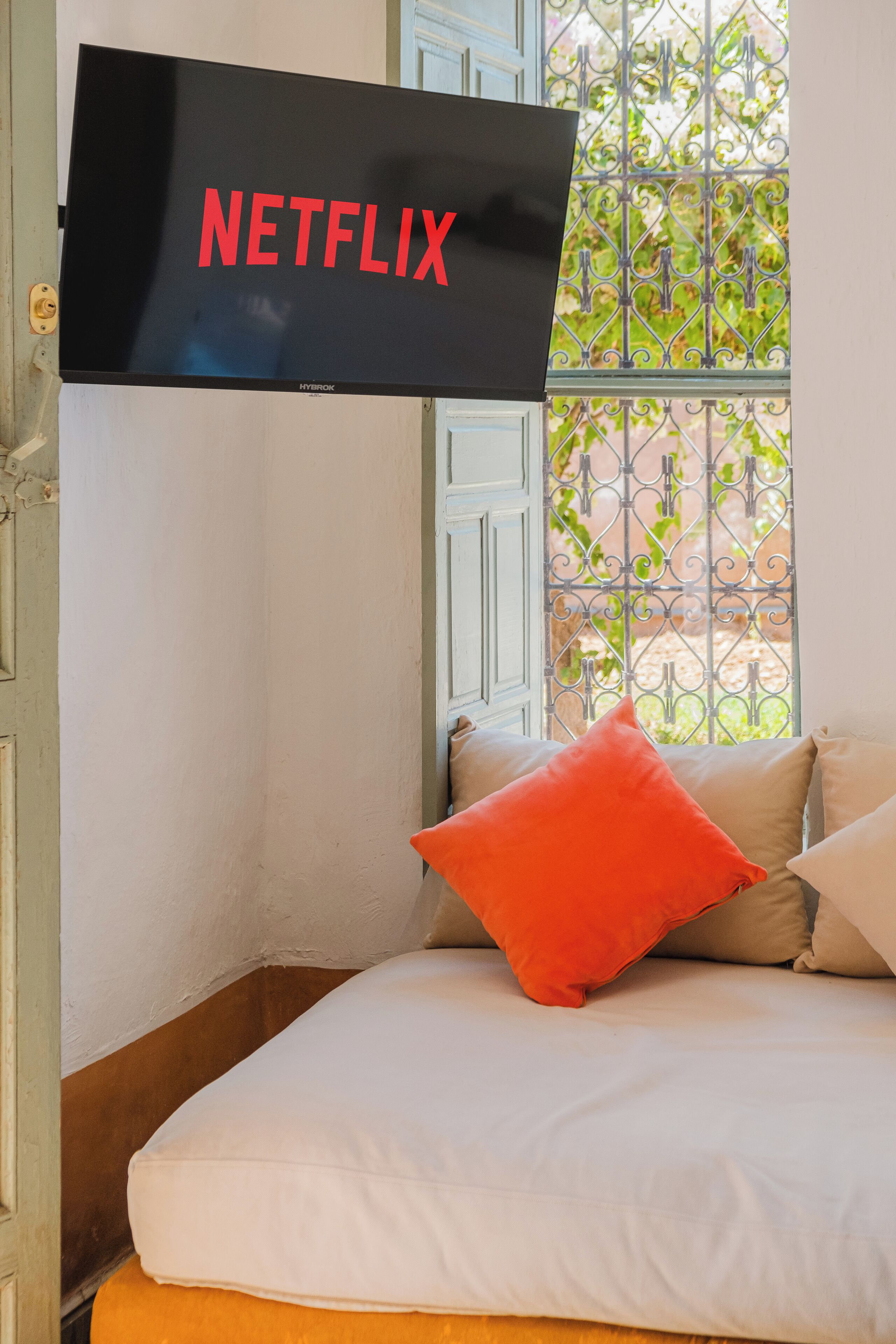 Une chambre à coucher avec un lit, une fenêtre avec des barreaux en métal et un téléviseur affichant le logo de Netflix.