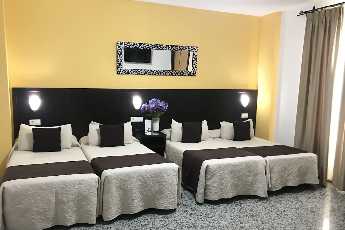 Une chambre d’hôtel avec deux lits, une tête de lit noire, un miroir fixé au mur et une petite table sur laquelle est posé un vase de fleurs.