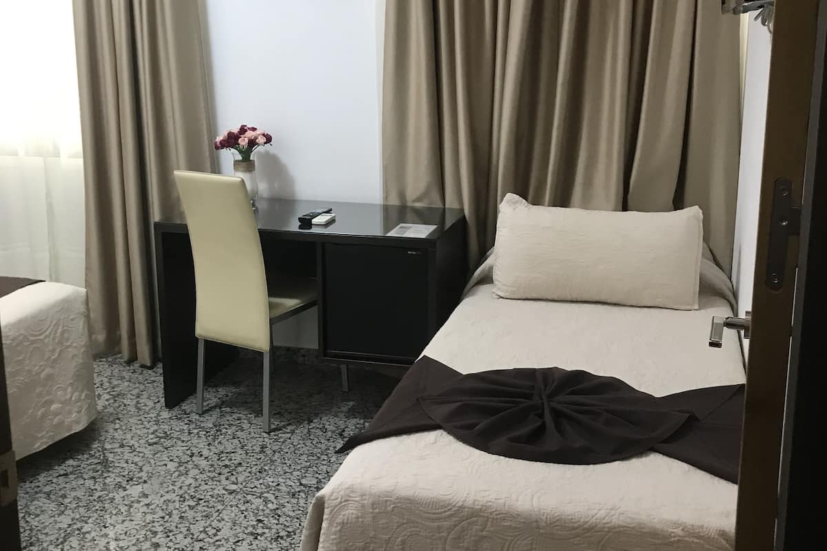 Une chambre d’hôtel avec un lit, un bureau, une chaise, une petite table et un tableau au mur.