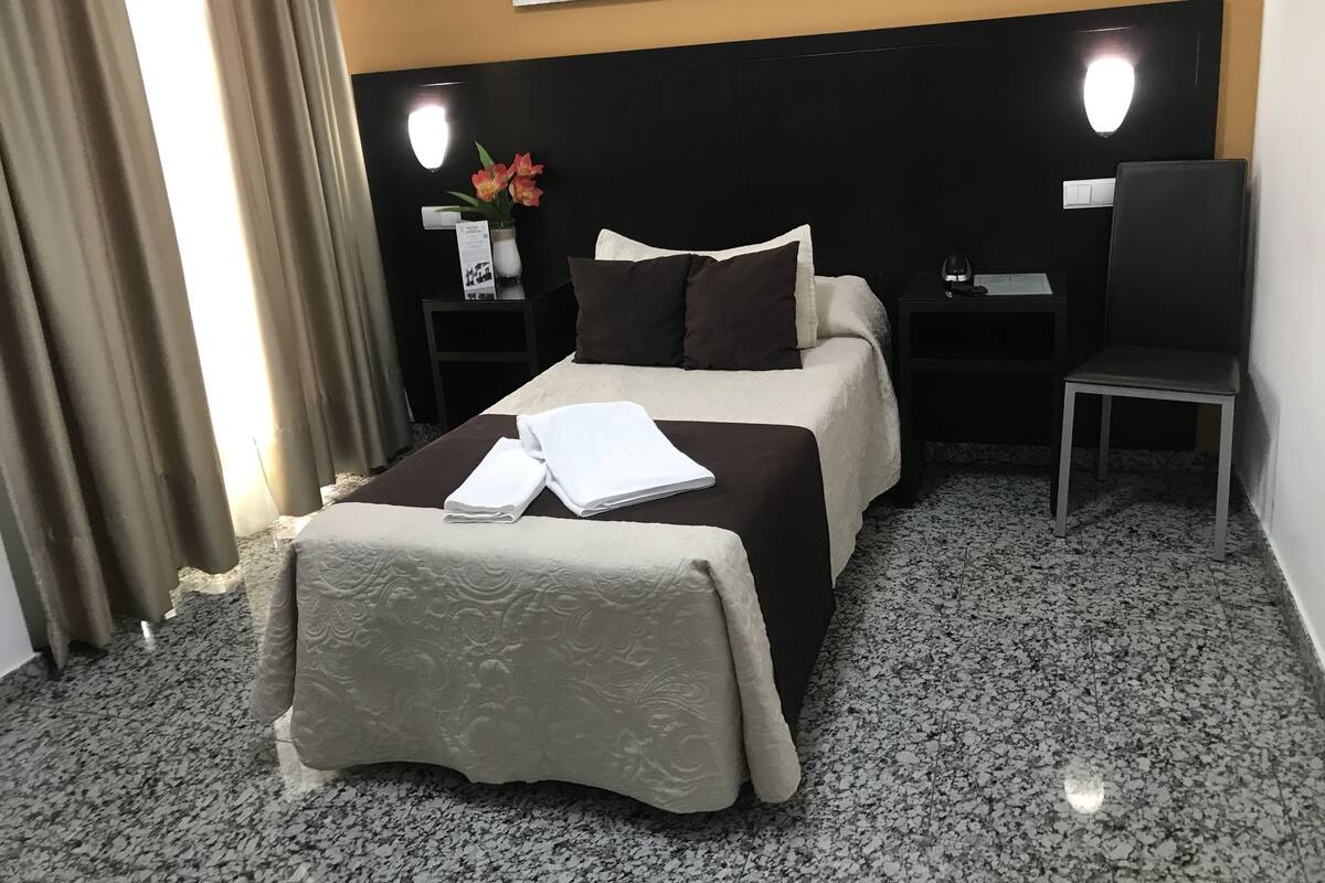 Une chambre d’hôtel comprenant un lit, un bureau, une chaise, une table de chevet et un miroir fixé au mur.