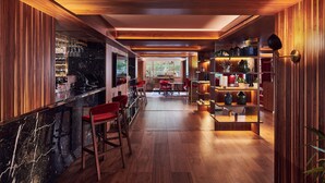A modern kitchen with wooden paneling, a marble countertop, and red bar stools. - The Level at the Melia White House (London)