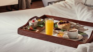 A hotel room with a bed, a bedside table, a tray with breakfast items, and a bathroom with a bathtub. - The Level at the Melia White House (London)