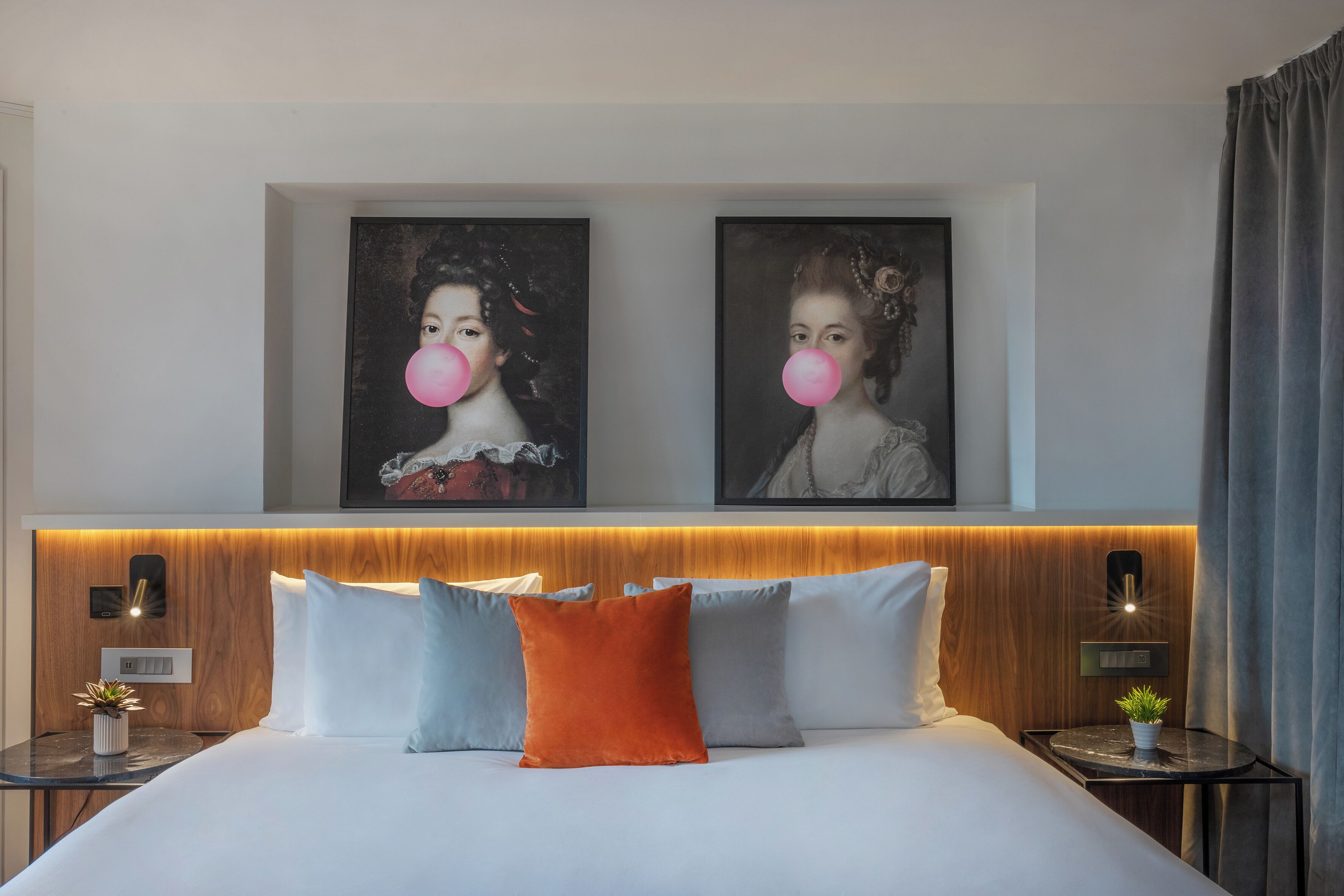 Una habitación de hotel moderna con una cama grande, dos mesitas de noche, un cabecero de madera y dos obras de arte enmarcadas en la pared.