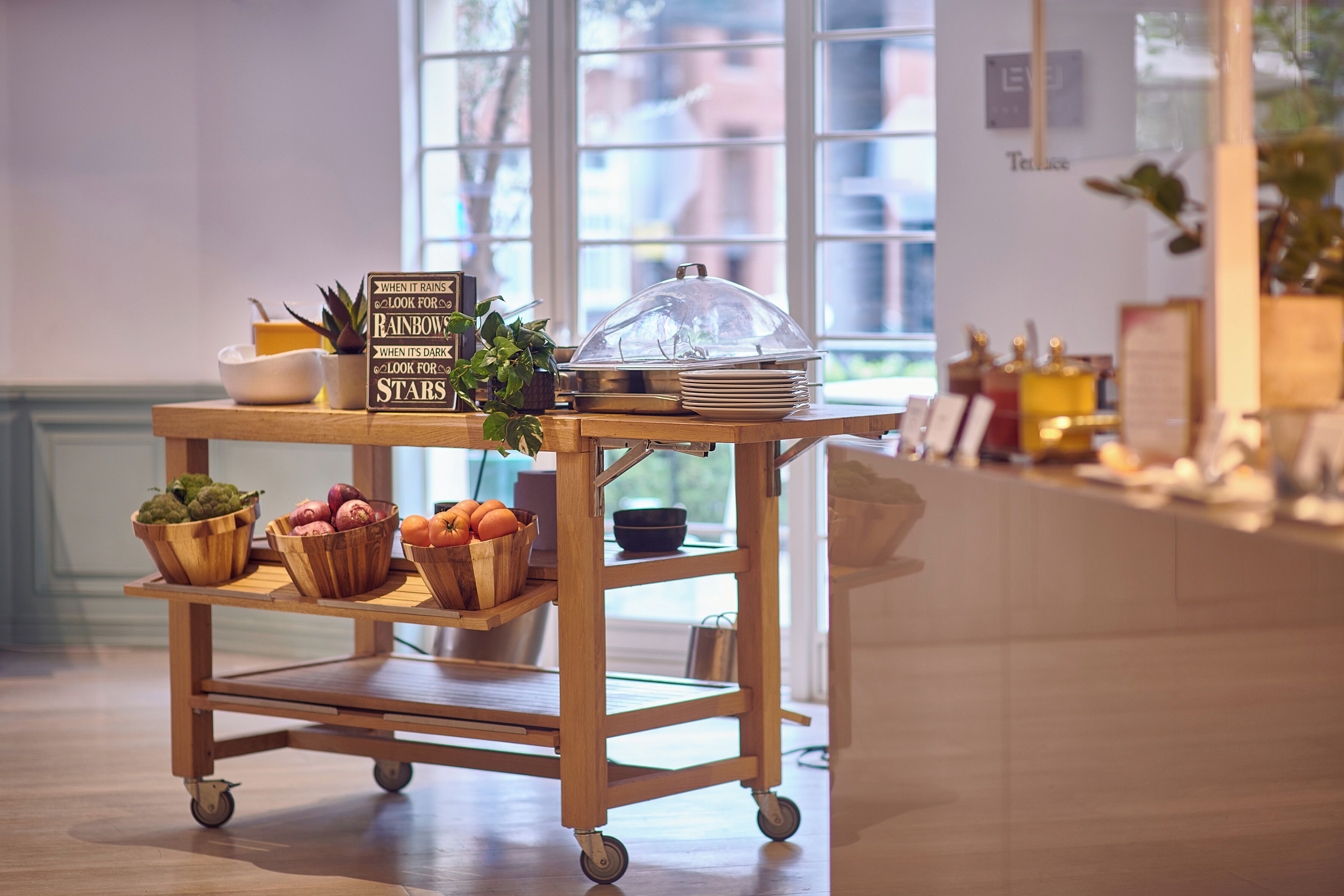 Un carro de madera con frutas, un letrero y una cubierta de vidrio abovedada en una habitación luminosa con ventanas grandes.