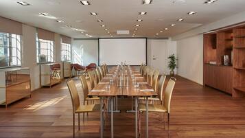 A conference room with a long table, chairs, a projector screen, and a wooden cabinet.