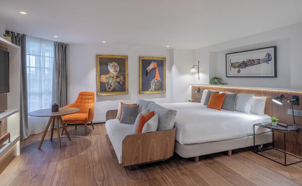 A modern hotel room with a sofa, a chair, a bed, and artwork on the walls. - The Level at the Melia White House (London)