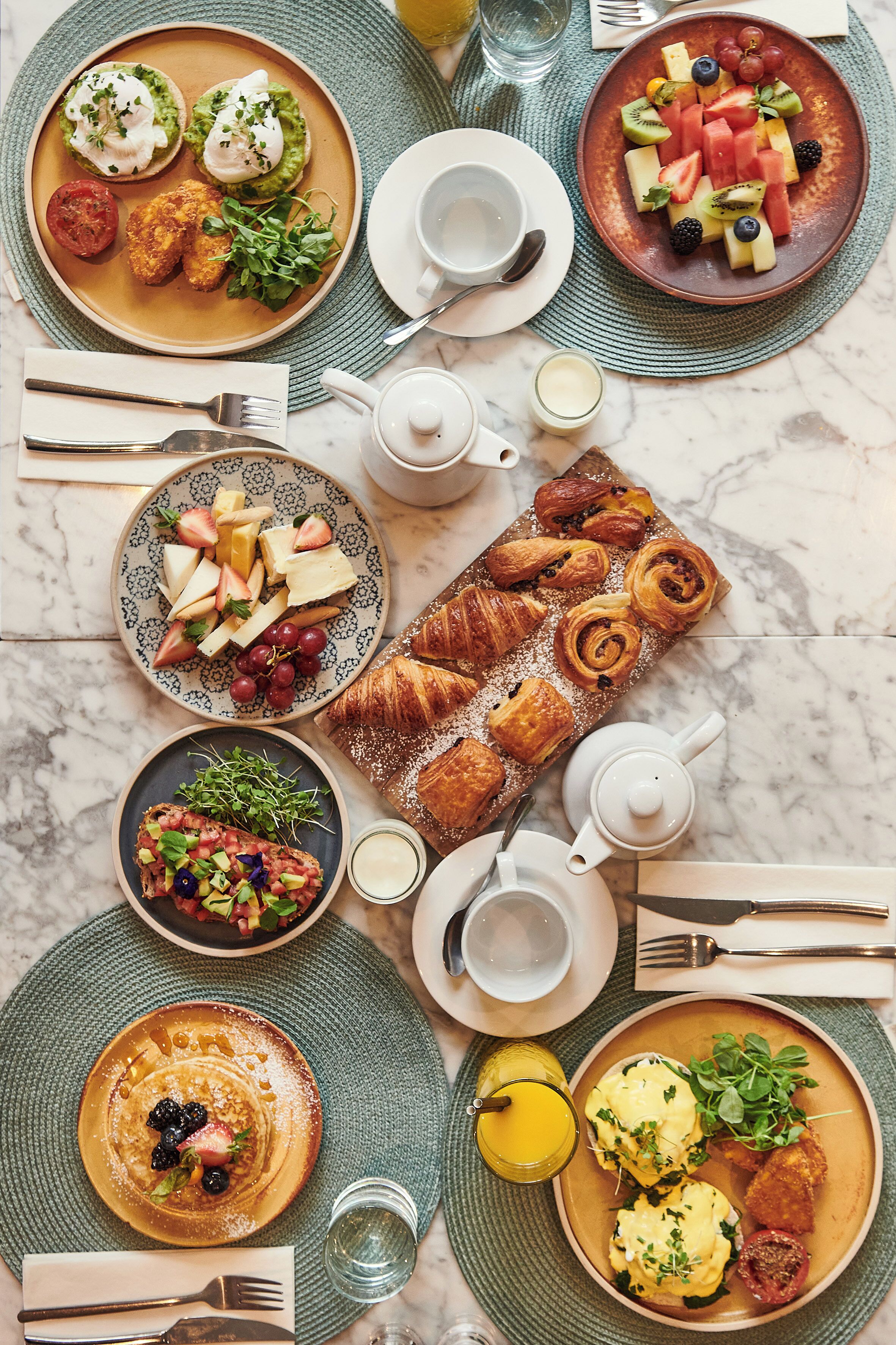 Un bufé de desayuno con una variedad de platos, como panqueques, croissants y fruta.