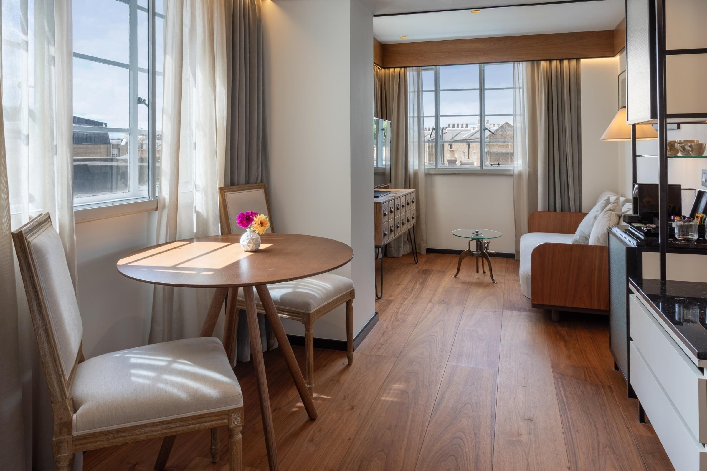 A hotel room with a dining table, two chairs, a sofa, a small side table, and a cabinet with drawers.