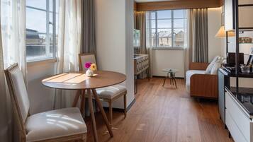 A hotel room with a dining table, two chairs, a sofa, a small side table, and a cabinet with drawers.