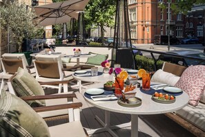 An outdoor seating area with round tables, chairs, and umbrellas. - The Level at the Melia White House (London)
