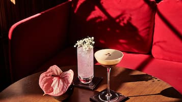 Una mesa con una bebida, un florero de vidrio con flores y una flor rosa sobre una mesa de madera en una habitación con un sofá rojo.