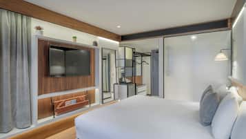 Una habitación de hotel moderna con una cama grande, un televisor de pantalla plana montado en un panel de madera, un escritorio pequeño con una silla y un espejo.