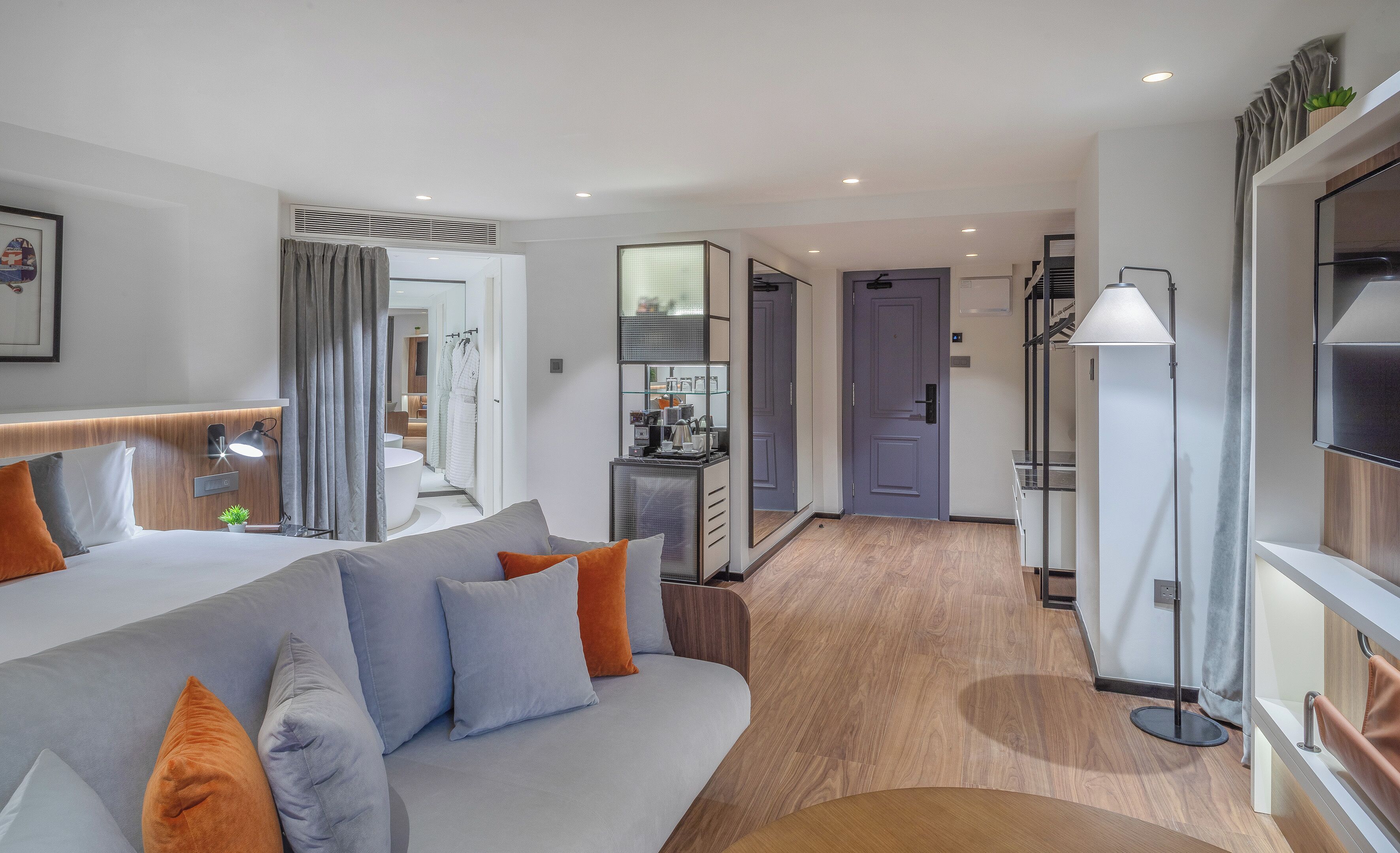 Una habitación de hotel moderna con una cama grande, un escritorio, un baño y vista al pasillo.