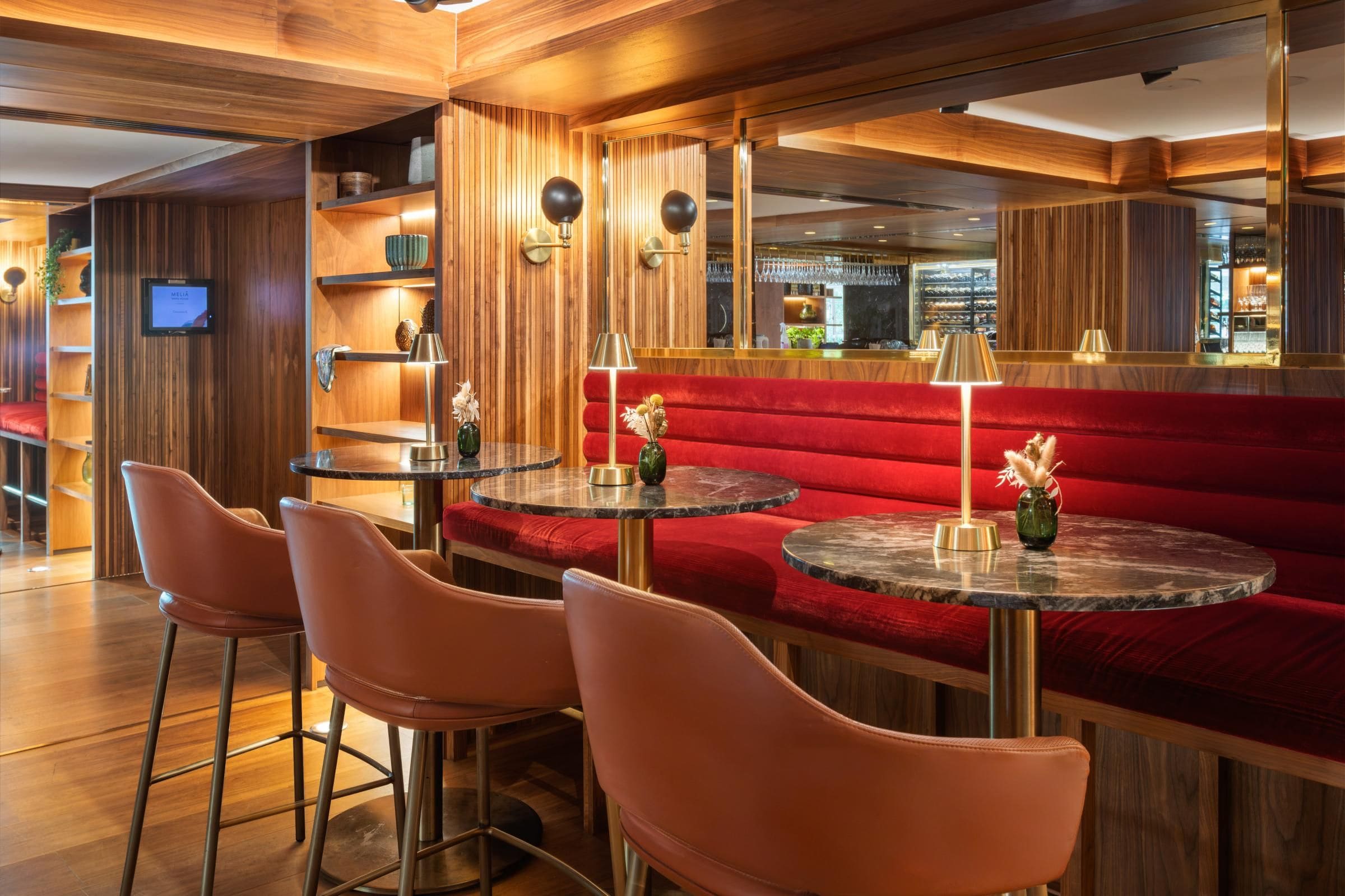 A bar area with red upholstered seating, round tables, and modern lighting fixtures.