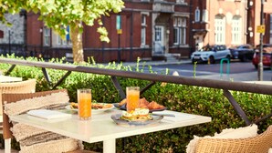 A table with breakfast items, a glass of orange juice, and a wicker chair. - The Level at the Melia White House (London)