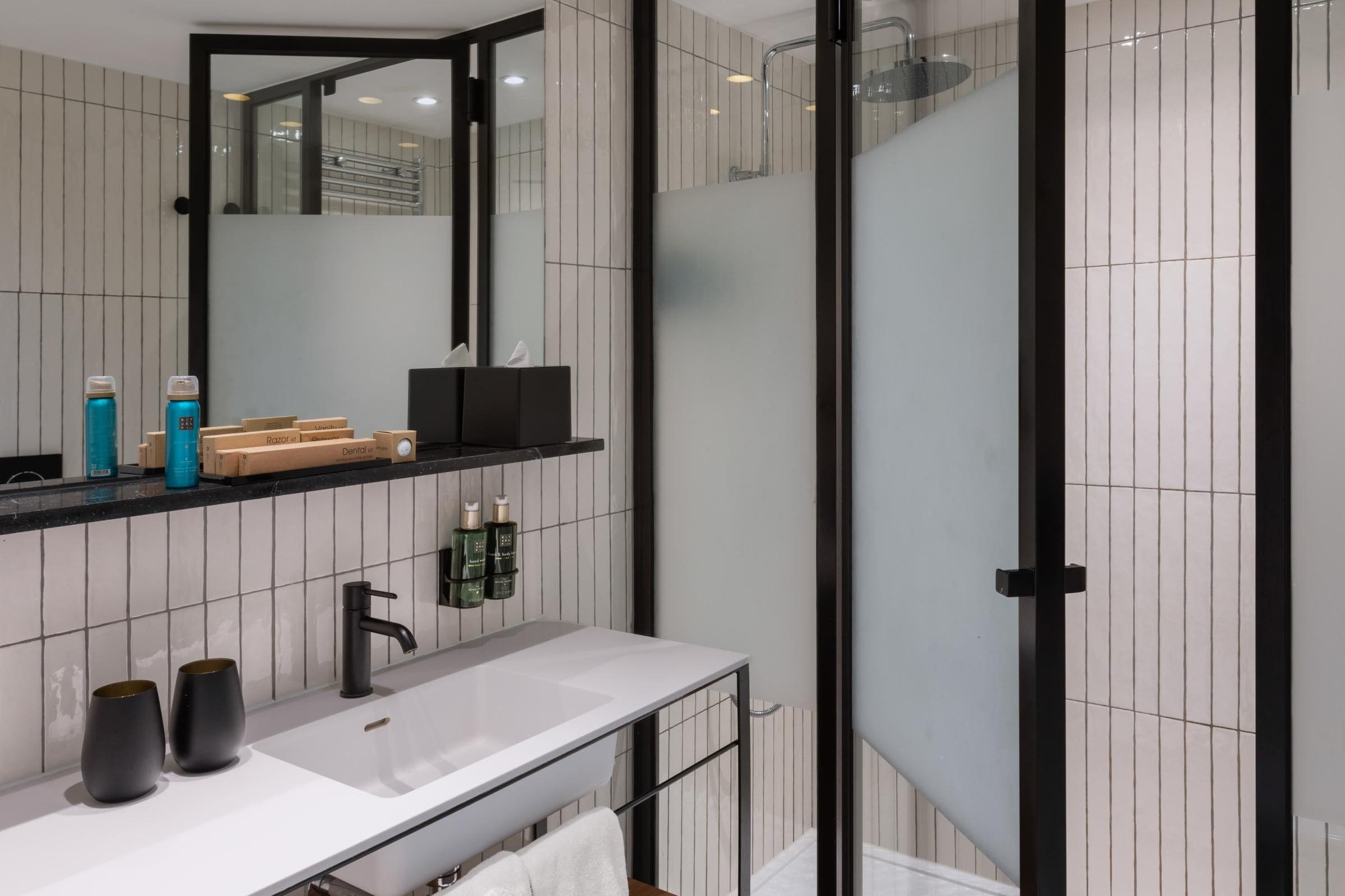 Un baño moderno con un espejo grande, un lavamanos blanco y una cabina de ducha de vidrio.