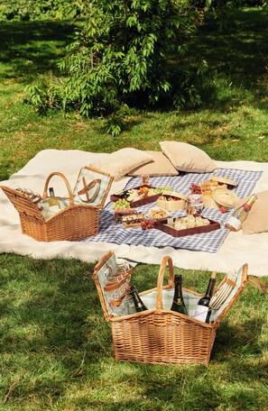 A picnic setup with a checkered blanket, wicker baskets, and food items on a grassy area. - The Level at the Melia White House (London)